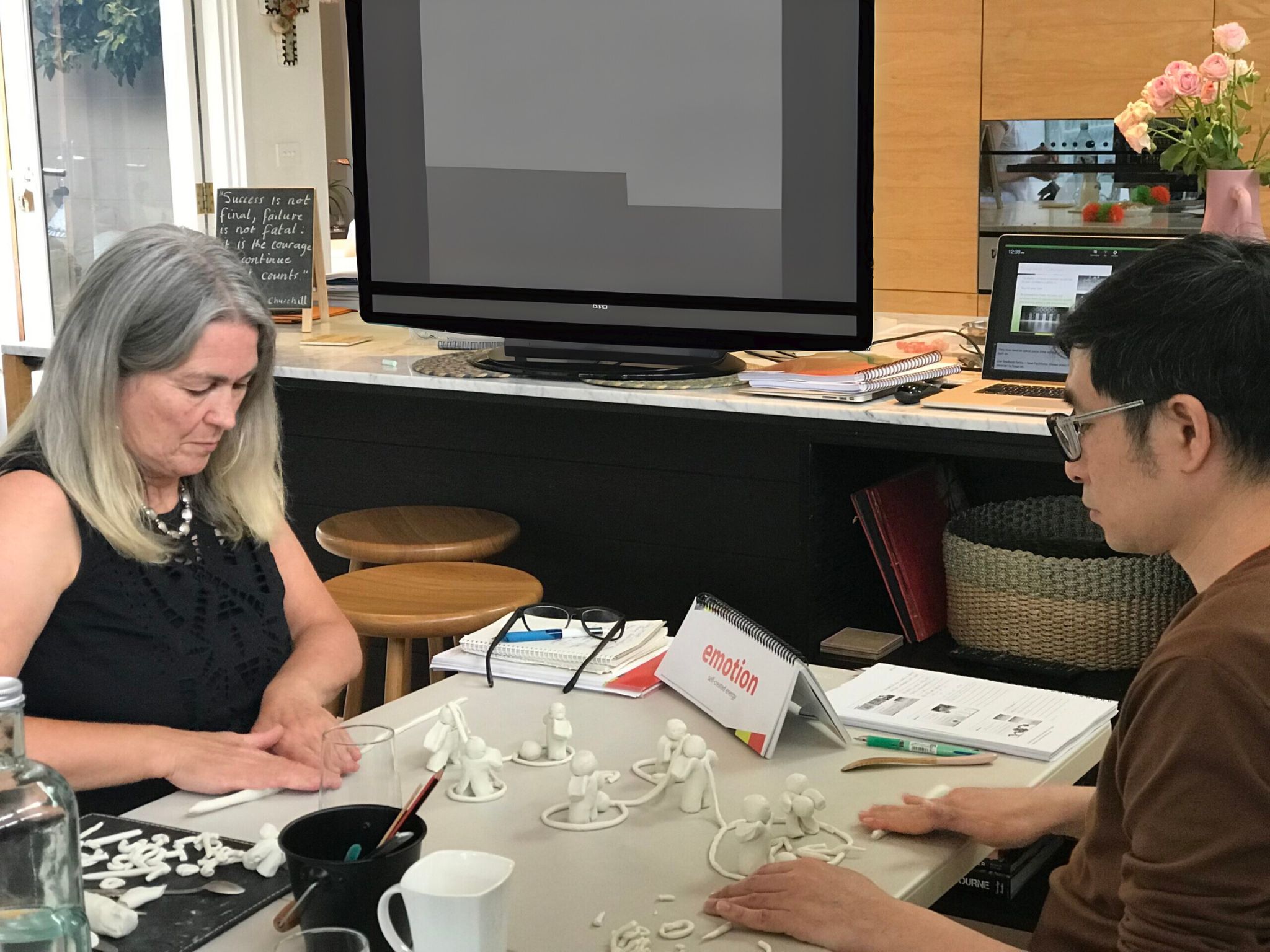 2 people sitting opposite each other, modelling life concepts with clay