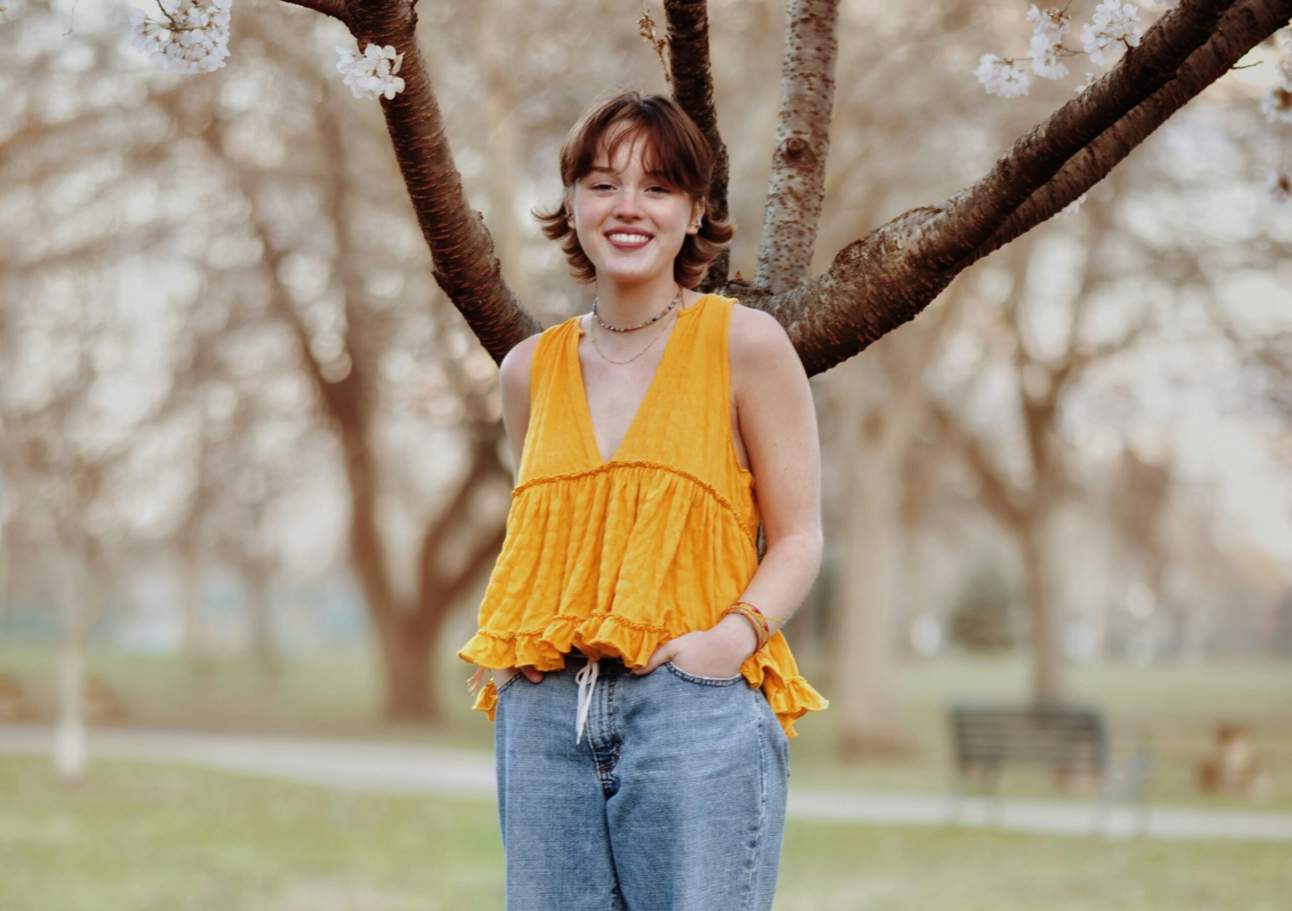 Young woman in yellow top smiling. Tree in background